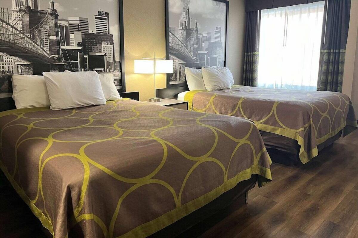 Une chambre d’hôtel avec deux lits, une fresque représentant un paysage urbain, une lampe et une fenêtre avec des rideaux.