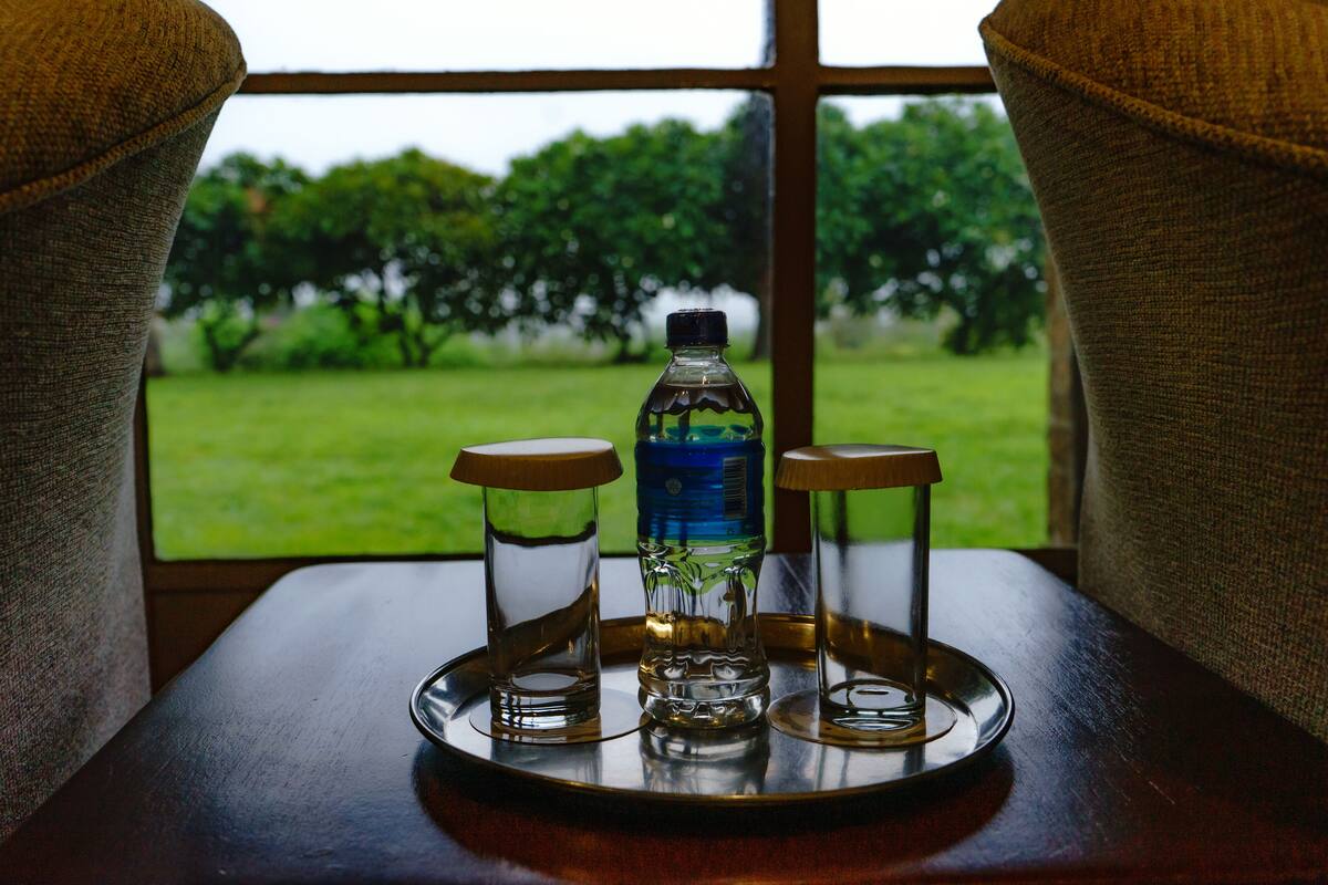 A tray with three glasses and a water bottle on a table by a window.