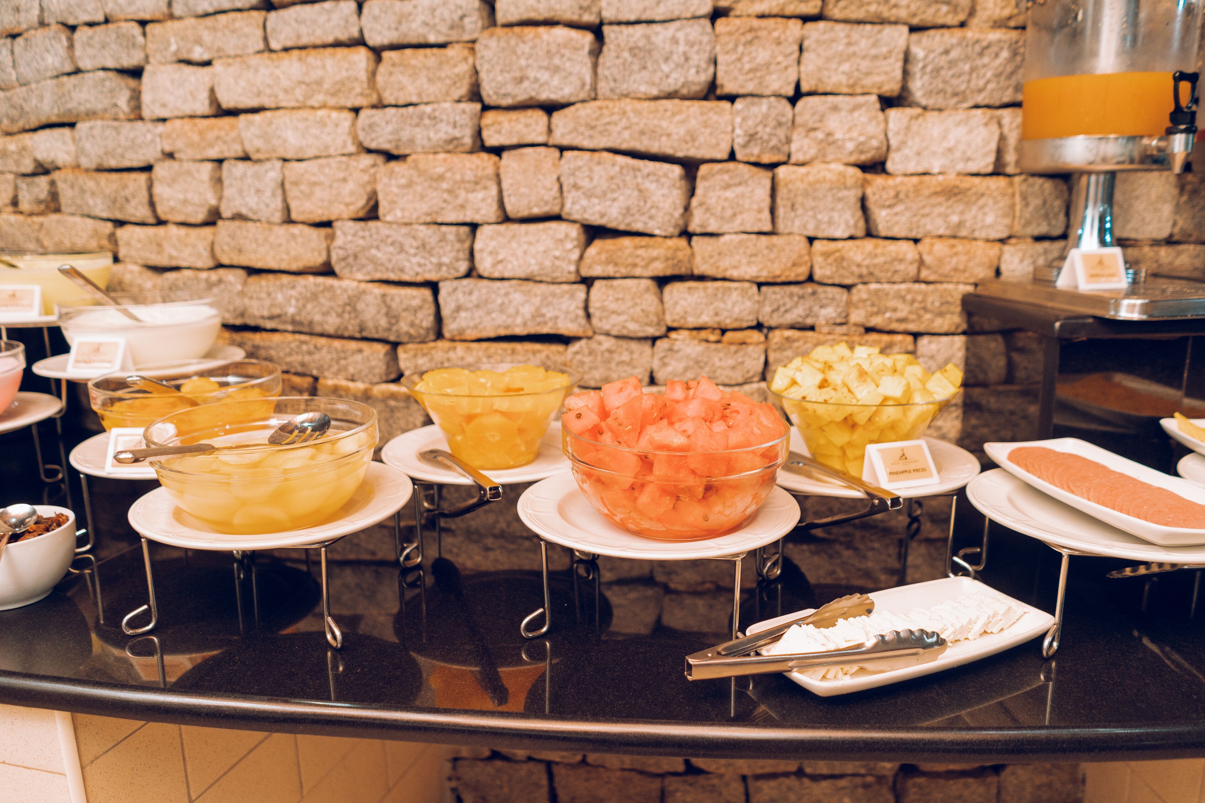 Un buffet con diversi cibi esposti su piatti e ciotole, con una parete in pietra sullo sfondo.