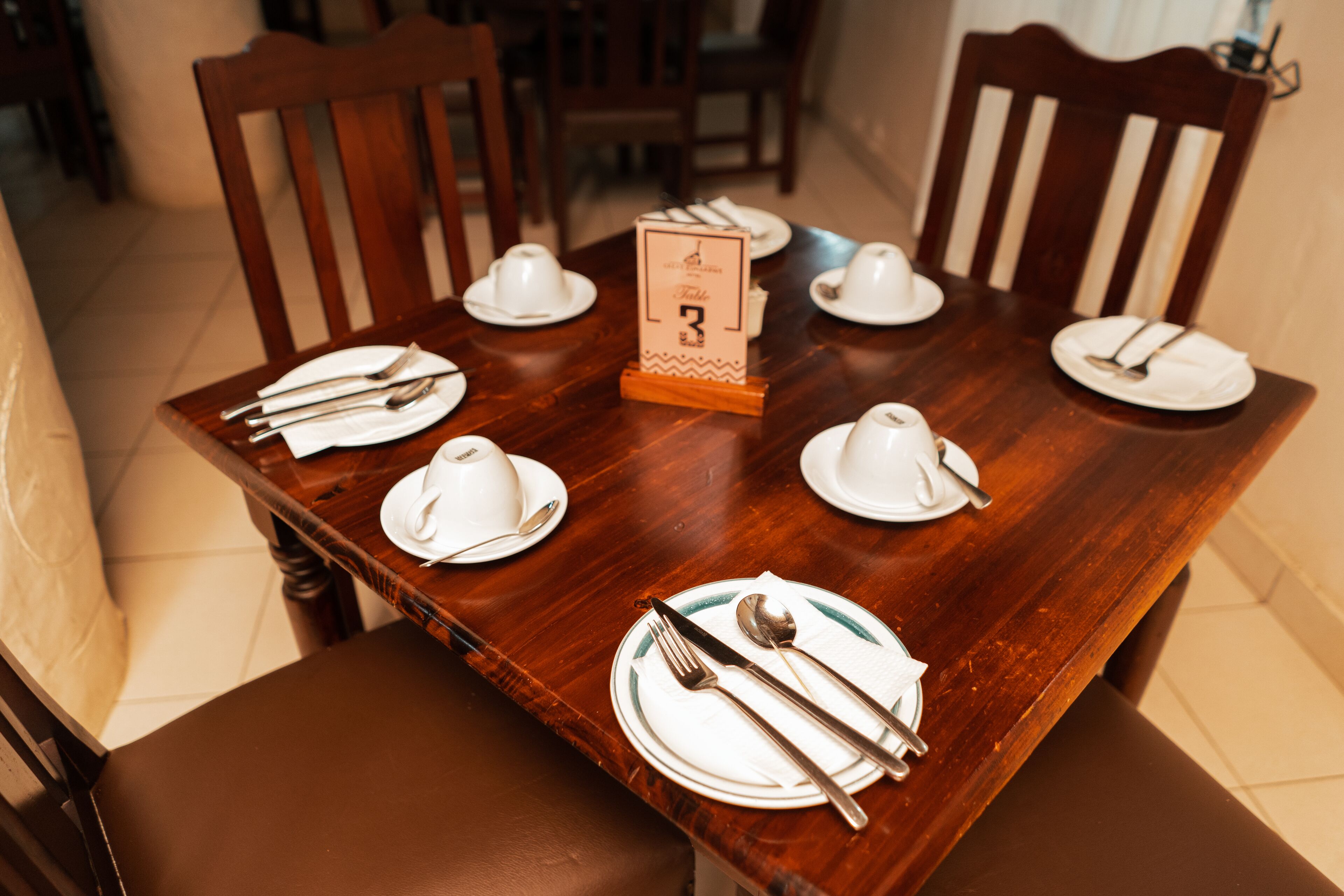 Tavolo da pranzo in legno apparecchiato per sei, con piatti bianchi, posate e un piccolo cartello con il numero 3.