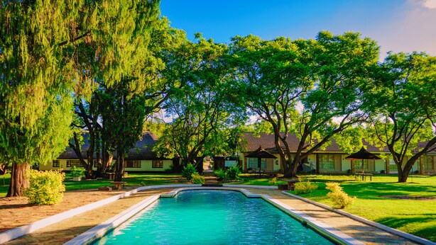 A swimming pool surrounded by trees and buildings. - Great Zimbabwe Hotel (Masvingo)