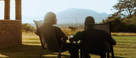 Two people sitting on chairs facing a brick structure with a view of mountains.