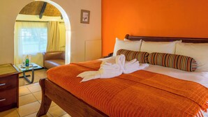 A hotel room with a bed, a wooden nightstand, a chair, and an arched doorway leading to another room. - Great Zimbabwe Hotel (Masvingo)