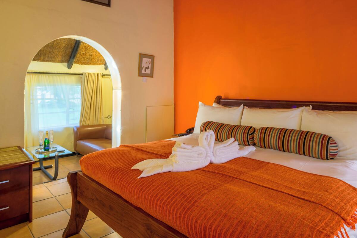A hotel room with a bed, a wooden nightstand, a chair, and an arched doorway leading to another room.