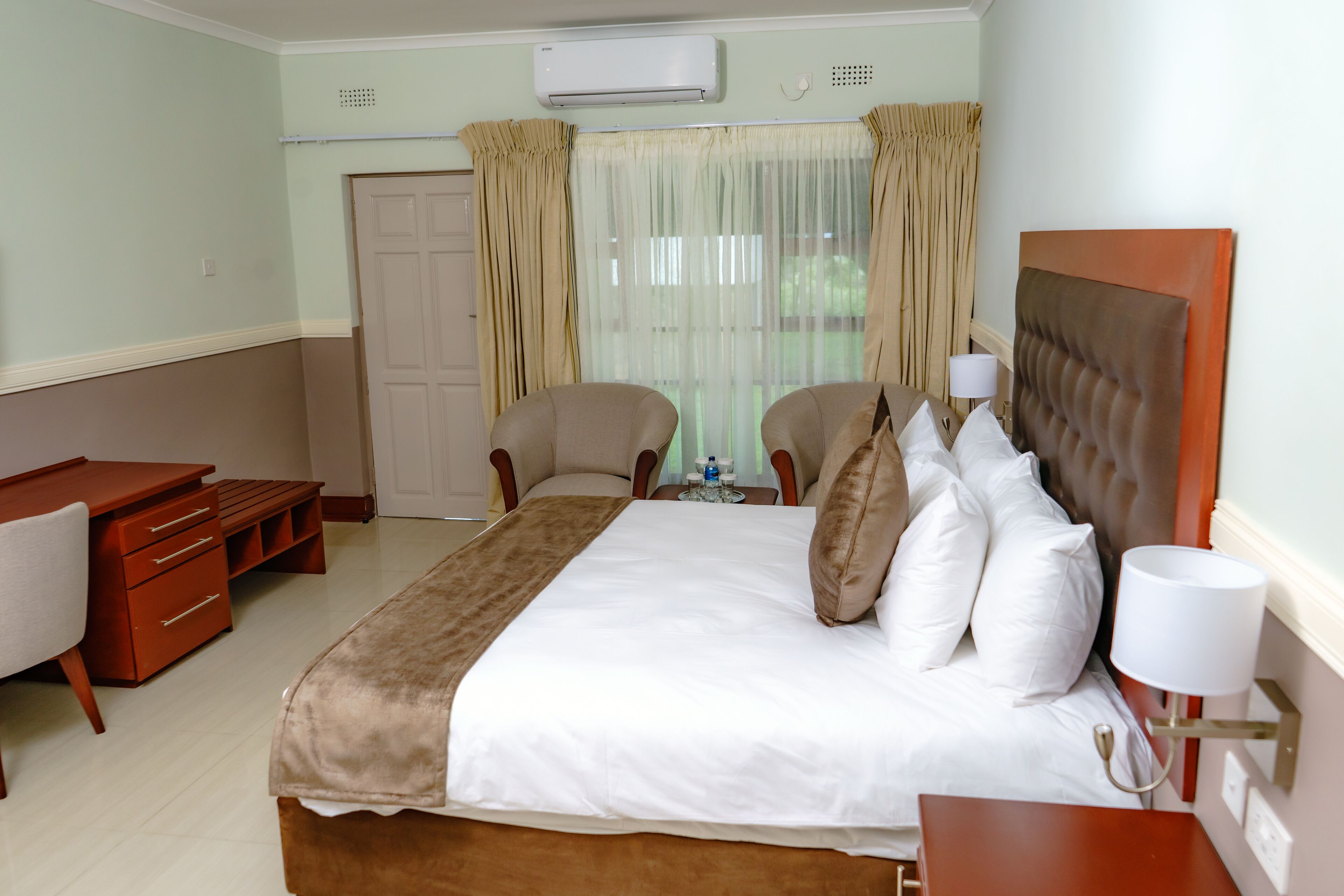 A hotel room with a bed, two chairs, a desk, and a bedside table.