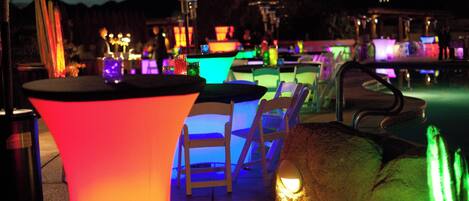 Een zwembadgedeelte met verlichte tafels en stoelen, een zwembad en een berg op de achtergrond.