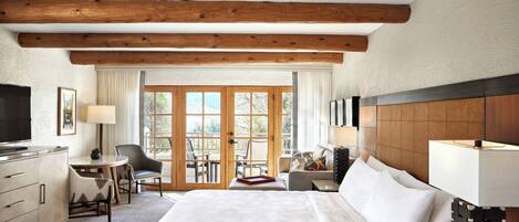 Habitación de hotel con una cama grande, un escritorio con televisor, una silla, un sofá y vistas al exterior a través de una puerta de cristal.