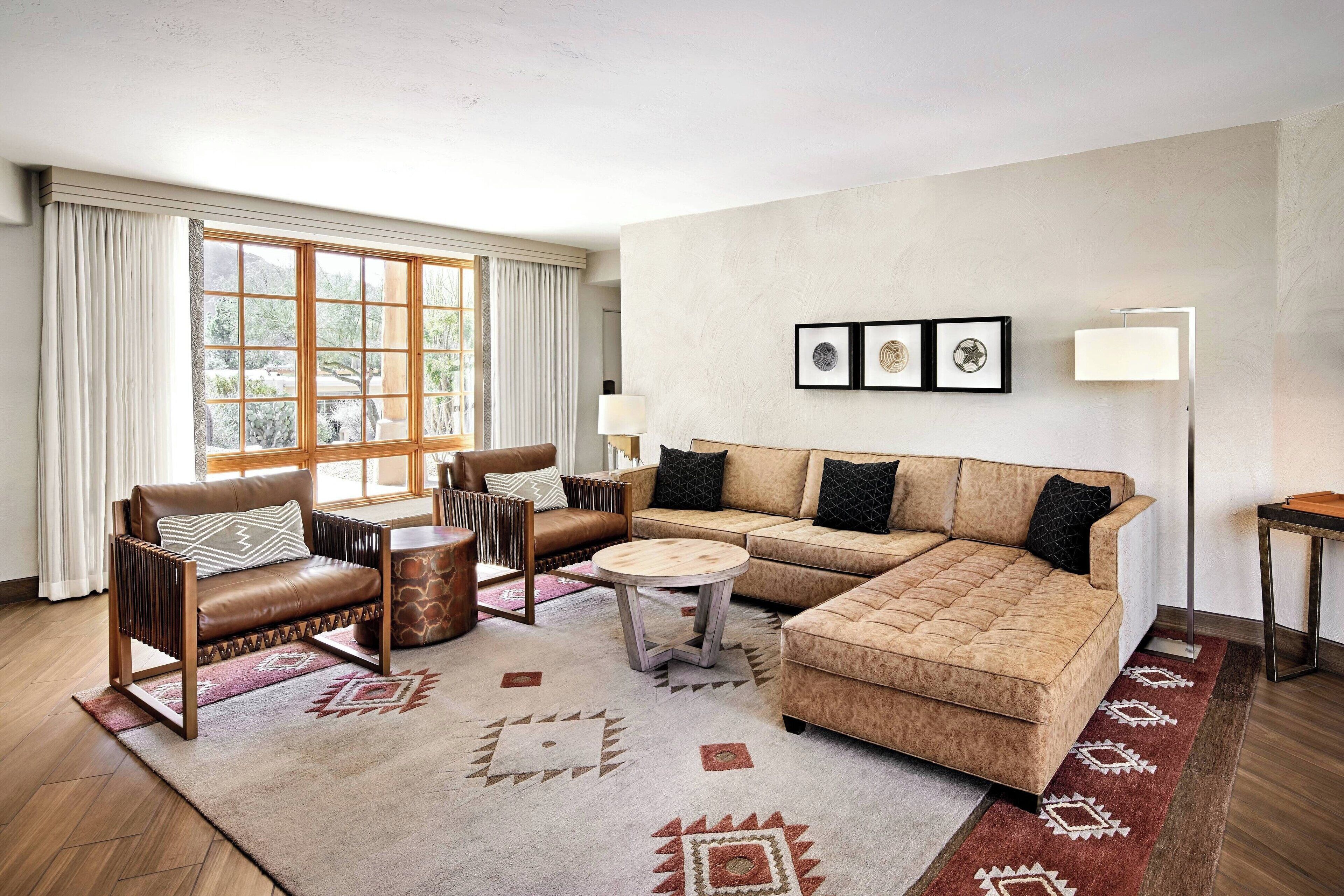 A living room with a brown leather sofa, a wooden coffee table, and a brown armchair with a patterned cushion. There are three framed pictures on the wall and a floor lamp on a side table.