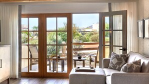 Une pièce comprenant un canapé, une petite table et donnant sur une terrasse extérieure grâce à de grandes portes vitrées.