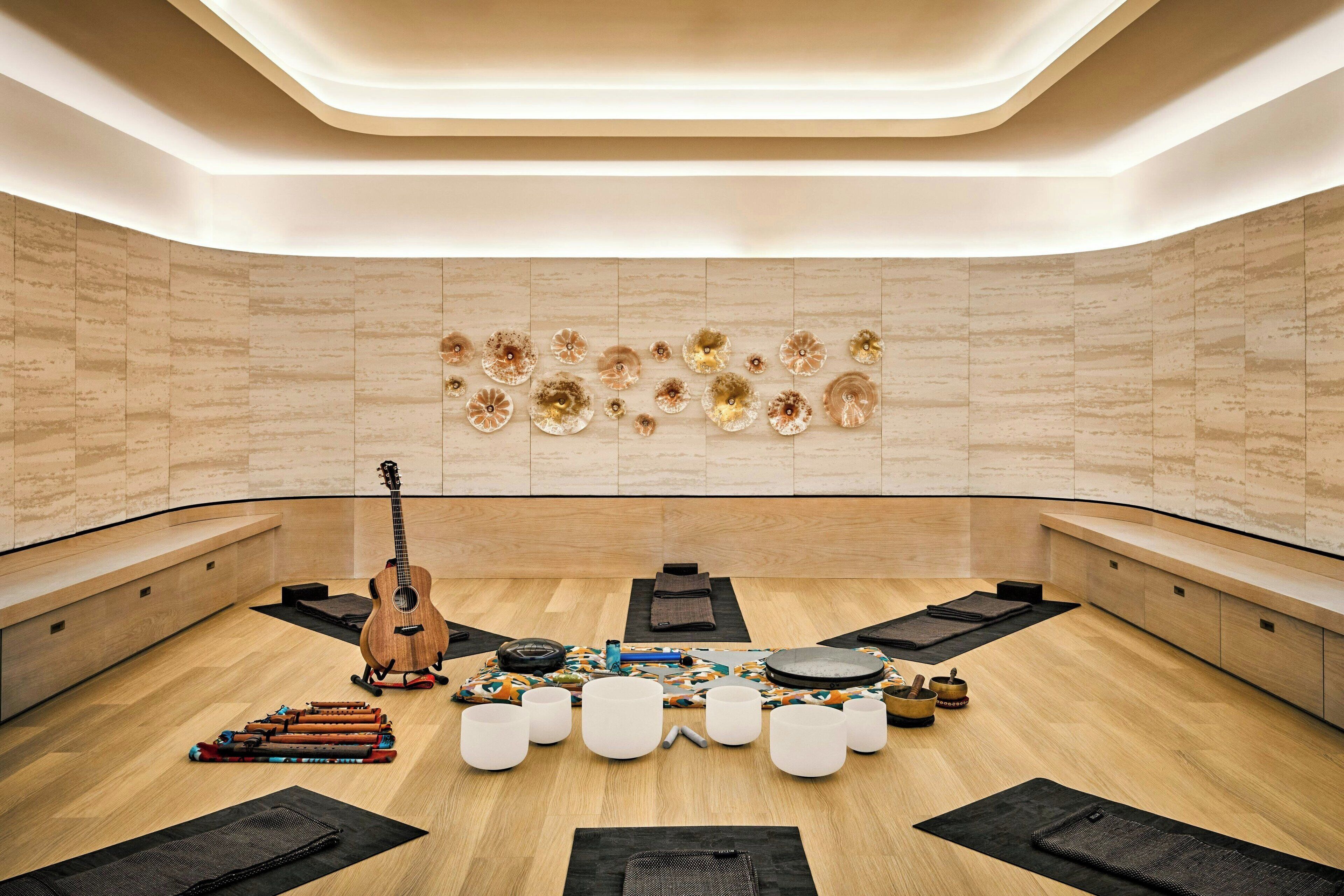 A modern spa room with a wooden floor, a guitar, meditation cushions, and a wall with decorative plates.