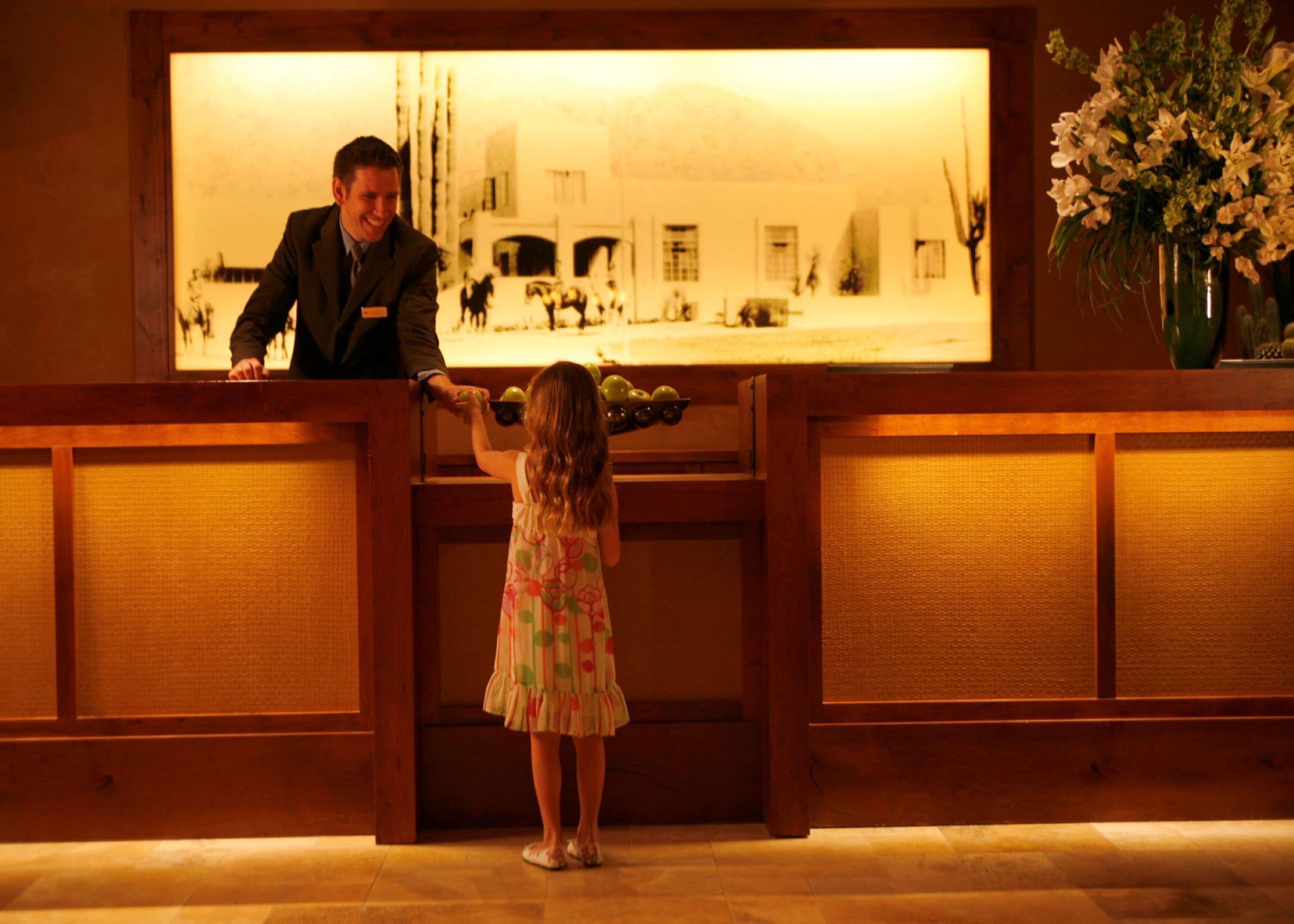 Una niña con un vestido floral está de pie en la recepción, interactuando con un hombre trajeado.
