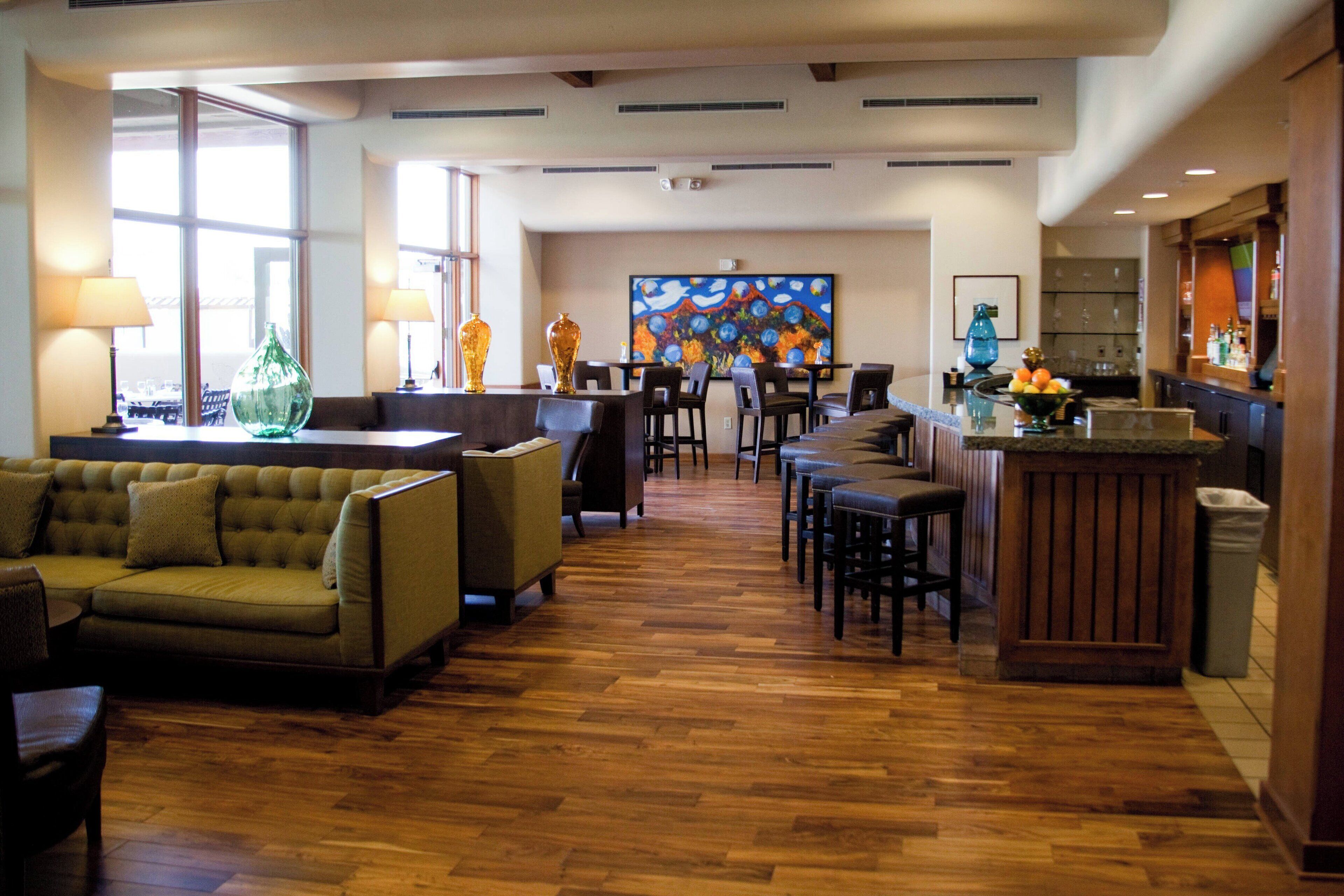 A spacious lobby with a wooden floor, a bar area, and a seating area with a sofa and chairs.