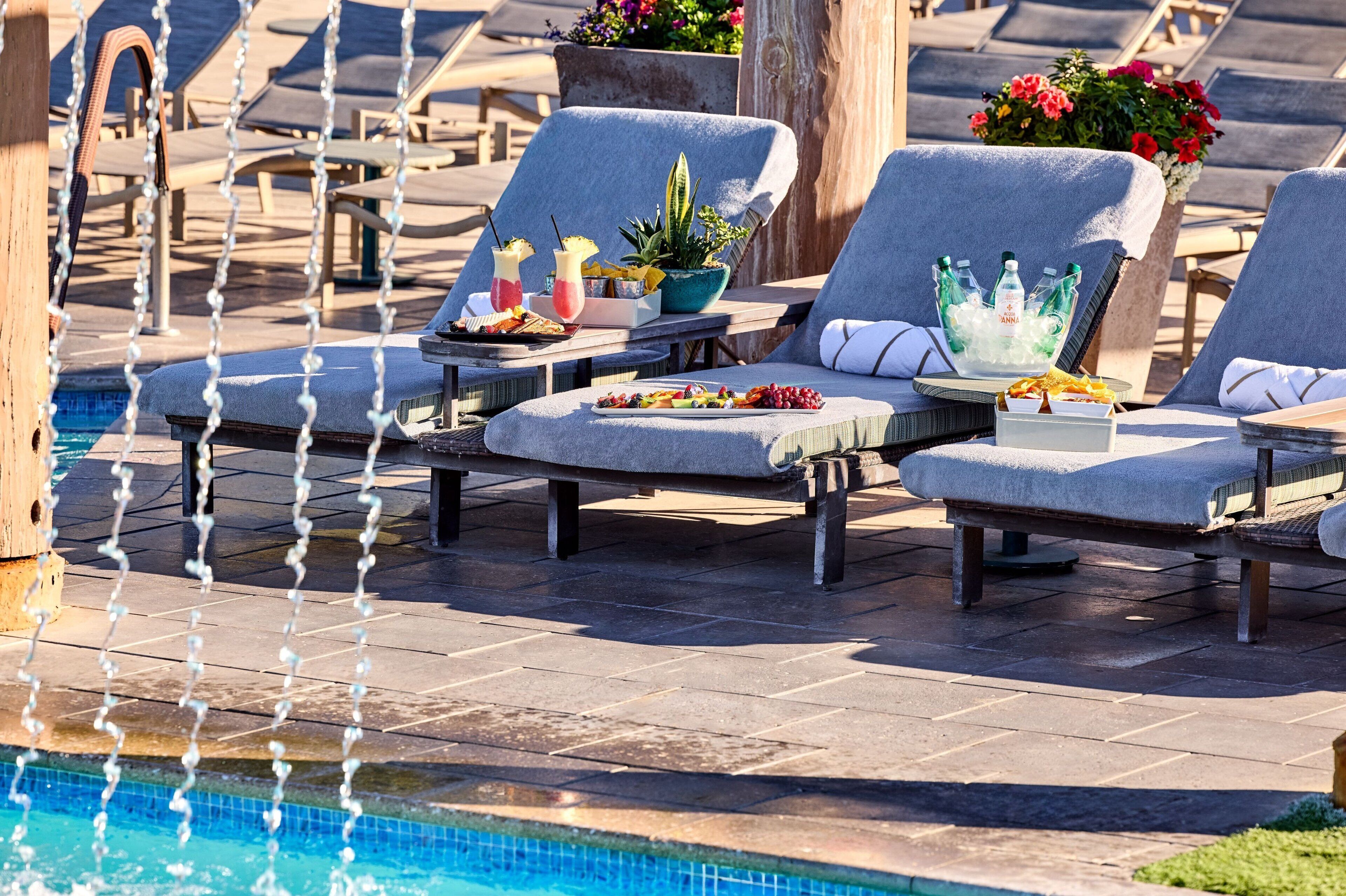 Un espace aménagé au bord de la piscine, avec des chaises longues, une table où sont servis des boissons et des en-cas, et une fontaine décorative.