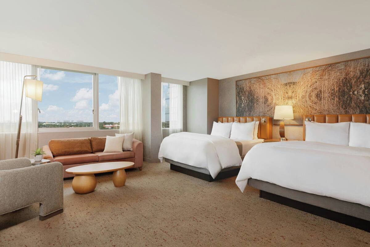 A hotel room with two beds, a sofa, a coffee table, and a large window with a view.