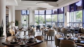 A modern restaurant with high ceilings, large windows, and a variety of seating arrangements including tables and chairs.