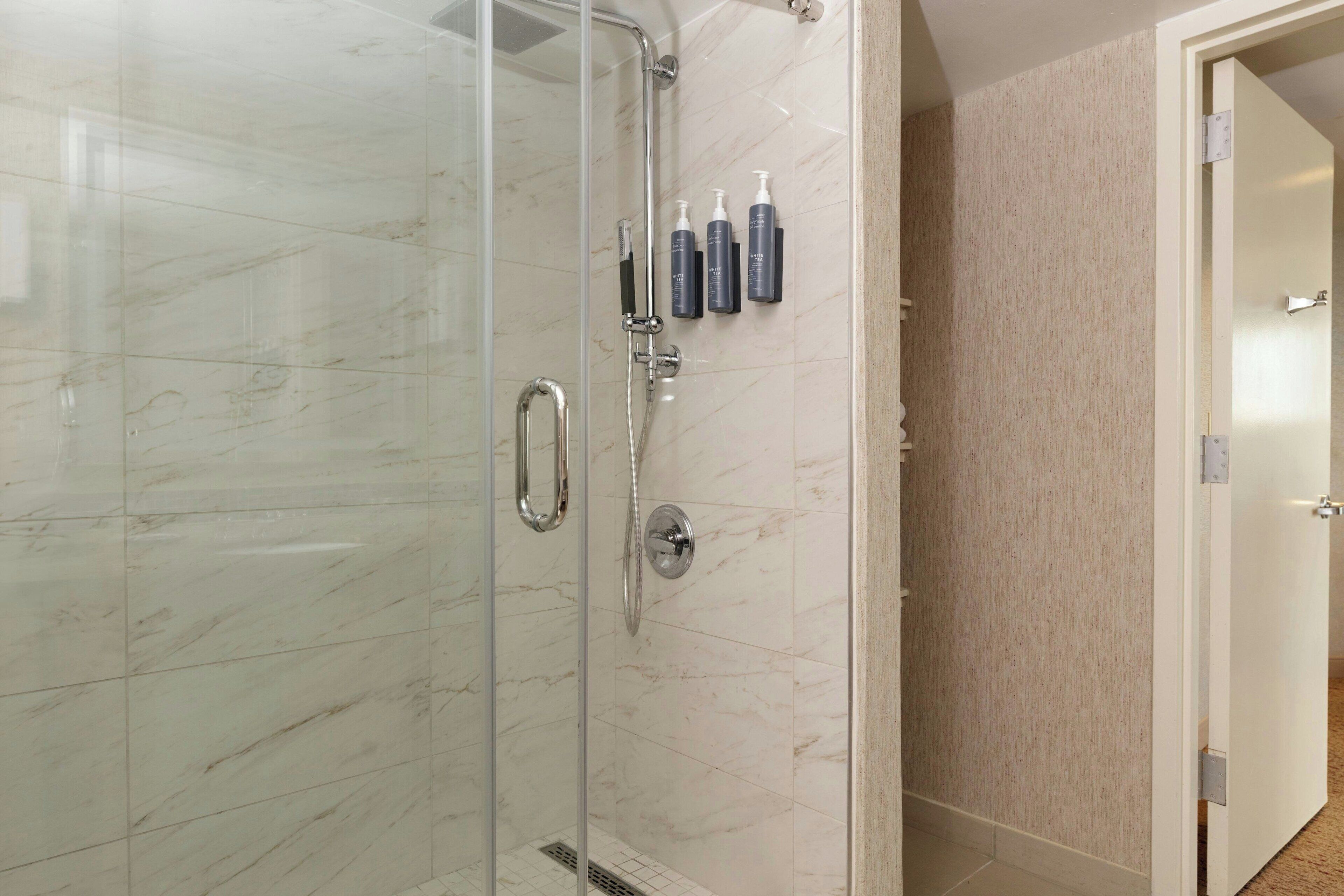 Un baño moderno con ducha envuelta en vidrio, baldosas de mármol y un juego de artículos de aseo en la pared.