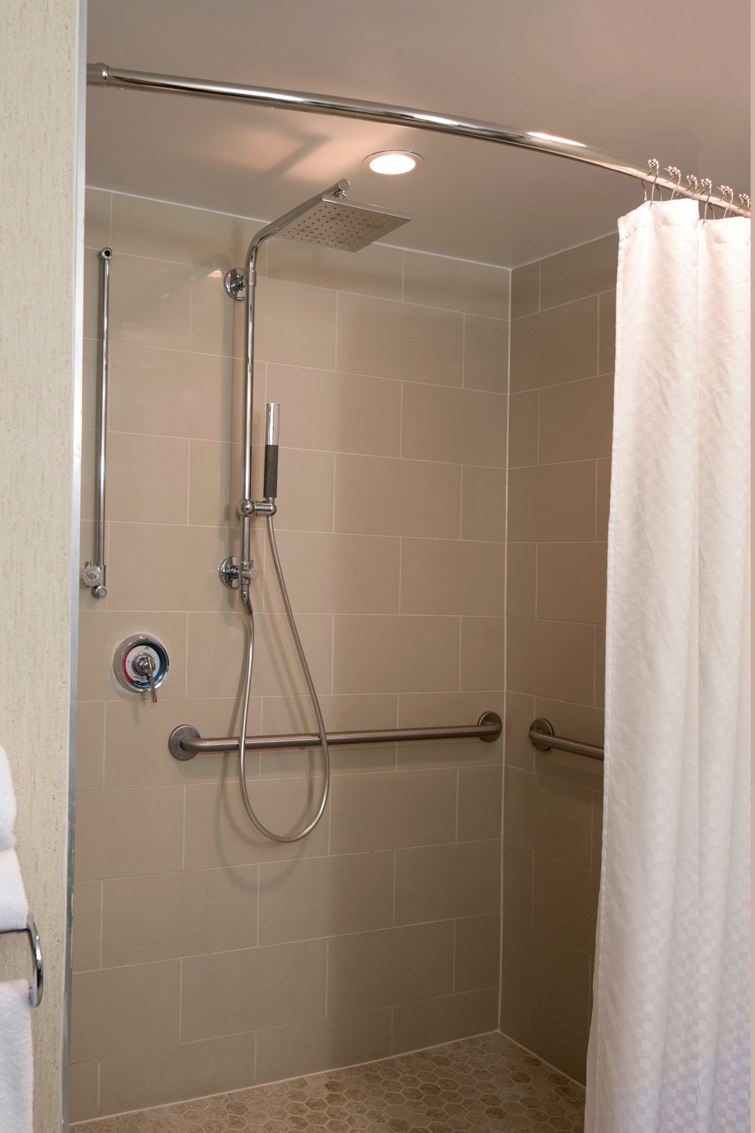 A shower area with a handheld showerhead, a handheld shower, and a grab bar.