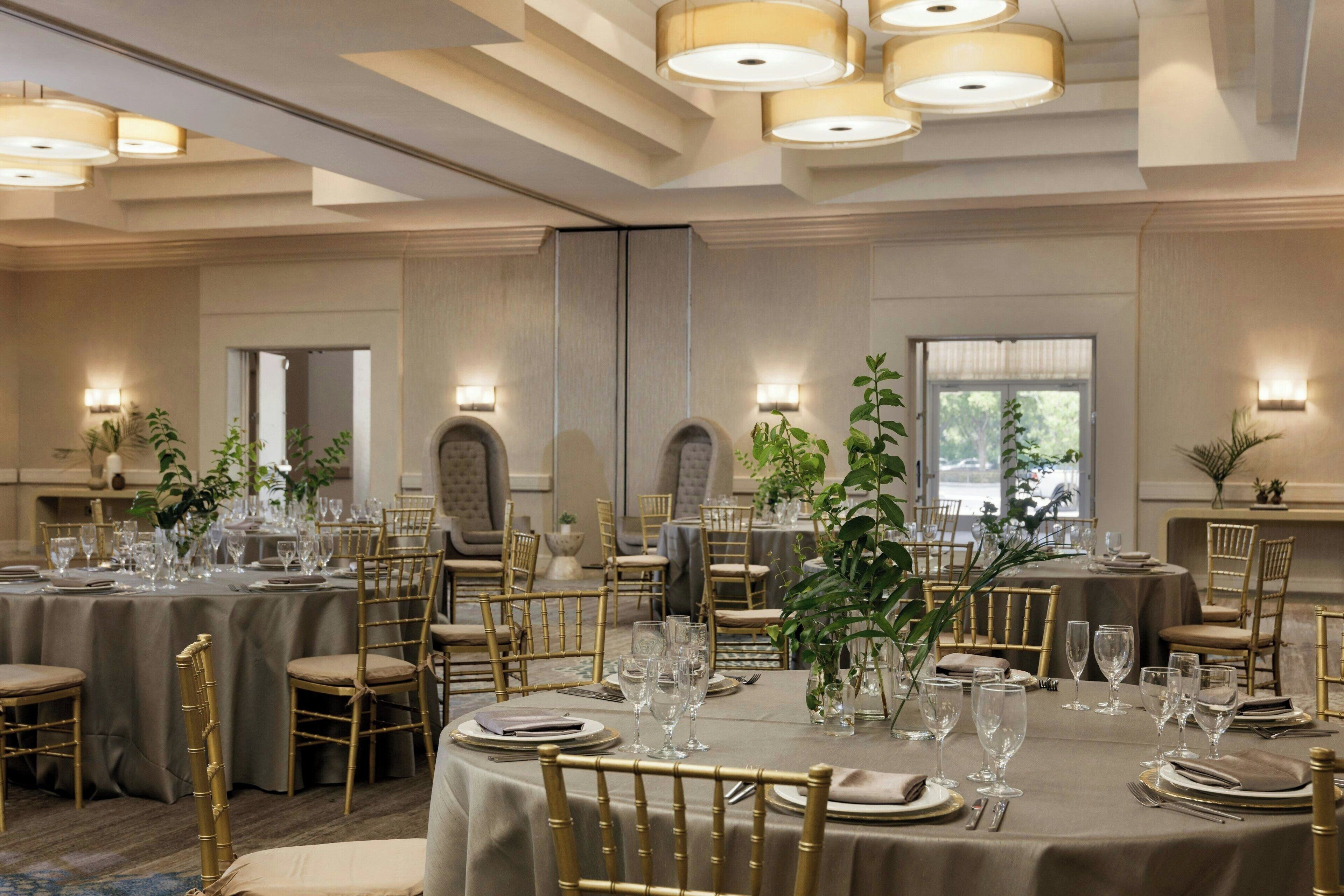 A banquet hall with round tables set for dining, gold chairs, and ambient lighting.