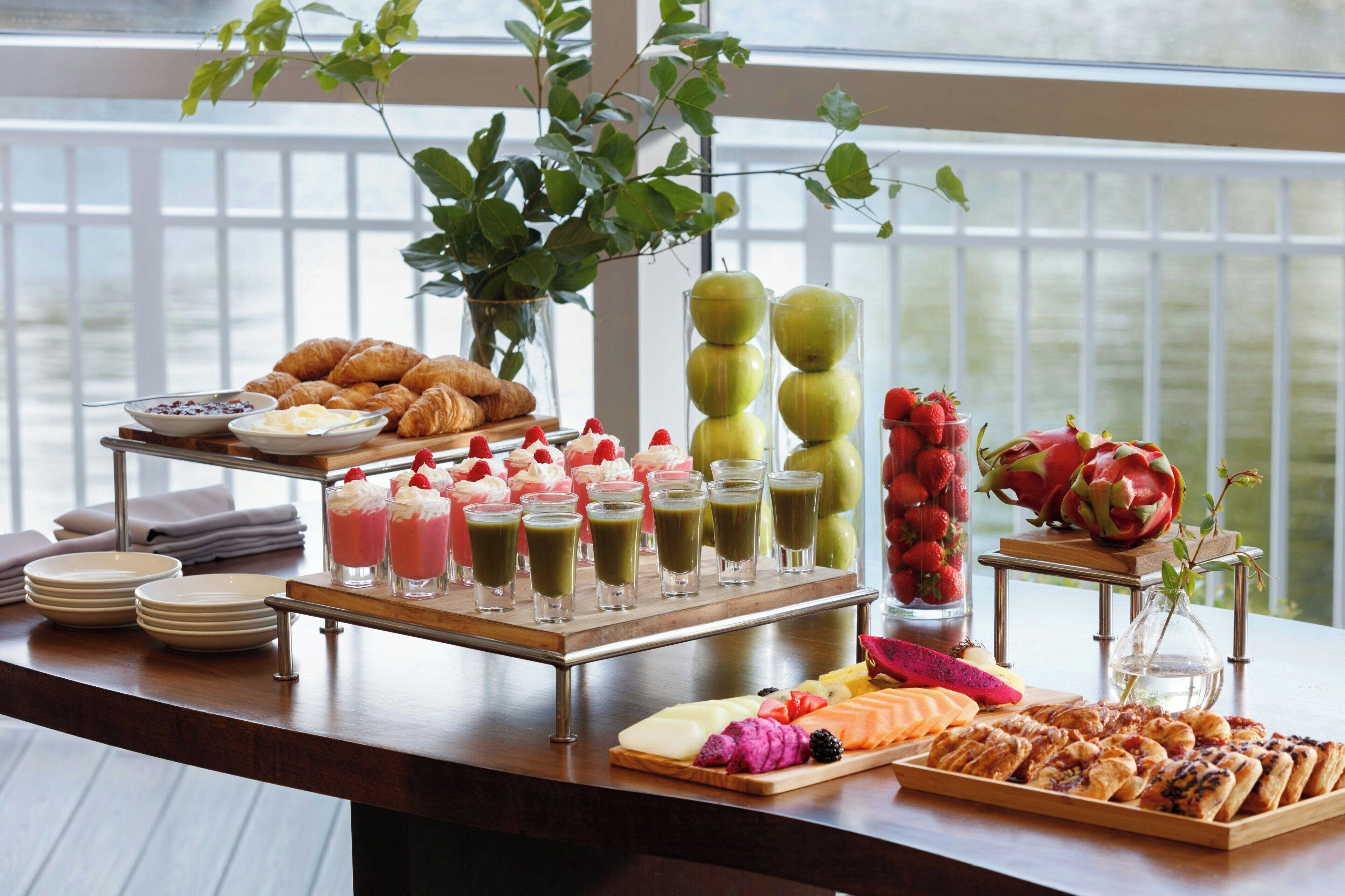 Une table de buffet proposant une variété d’aliments, notamment des pâtisseries, des fruits et des boissons.