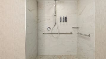 Una ducha a nivel con un cabezal de ducha de mano y dos botellas de champú y acondicionador en la pared.