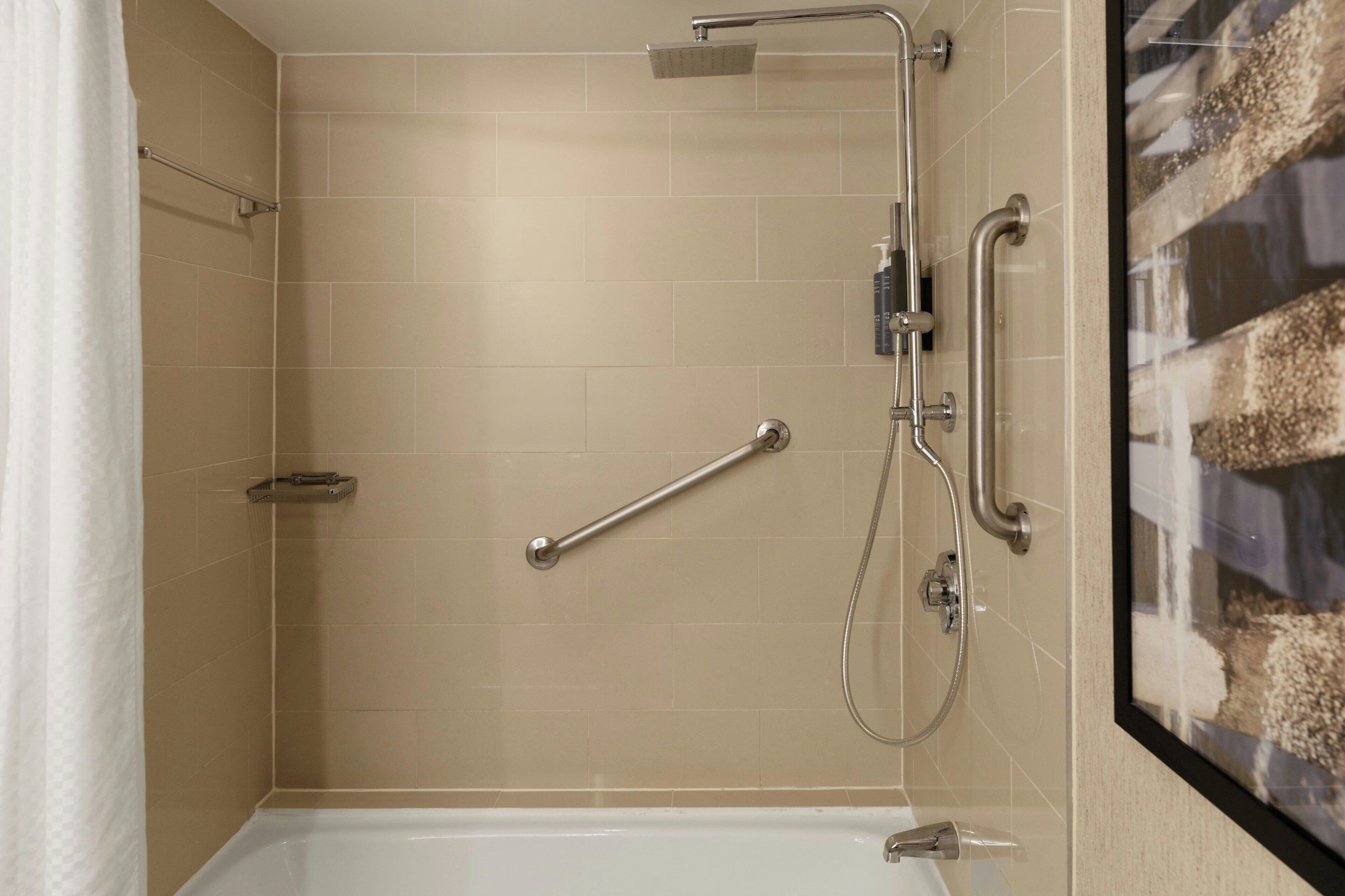 A bathroom with a shower, grab bars, and a bathtub.