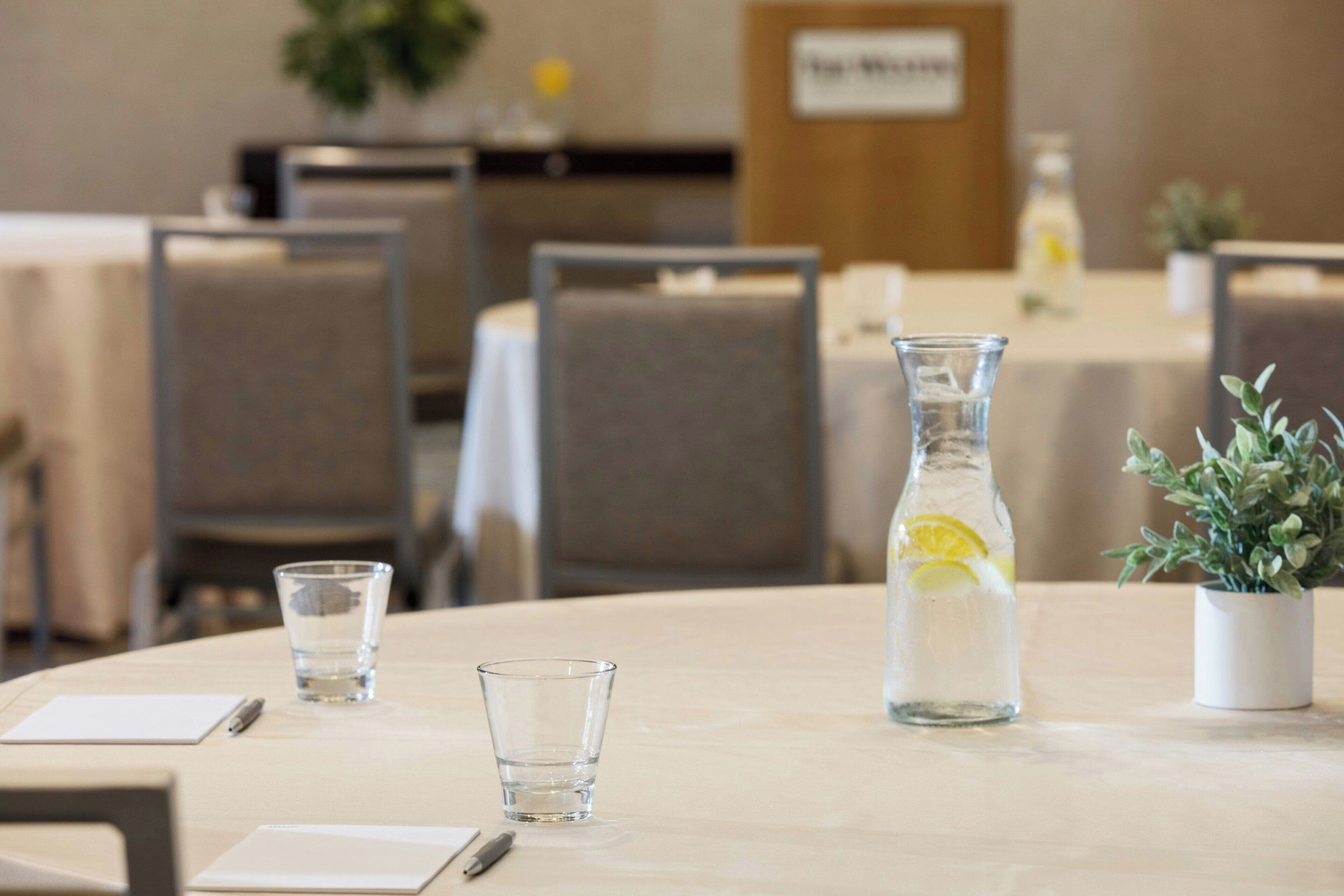 Un salón de conferencias con mesas, sillas, una botella de agua y una pequeña planta en maceta.