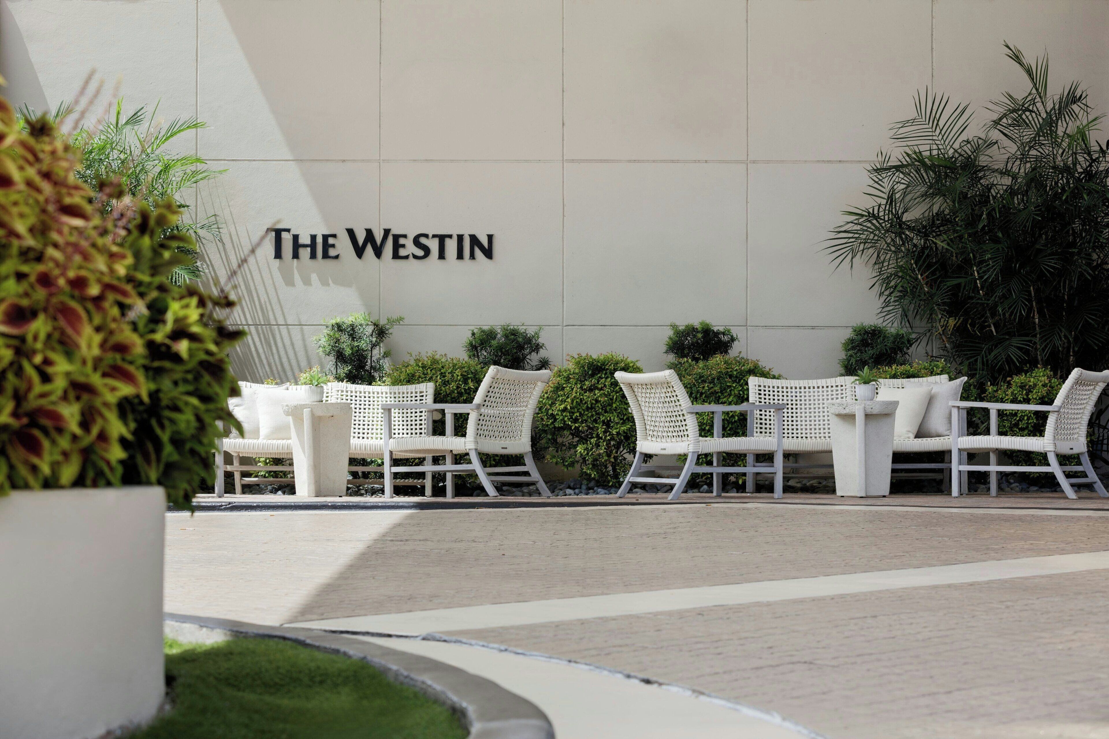 Uma área de estar com móveis de vime branco e uma placa com a inscrição 'The Westin'.