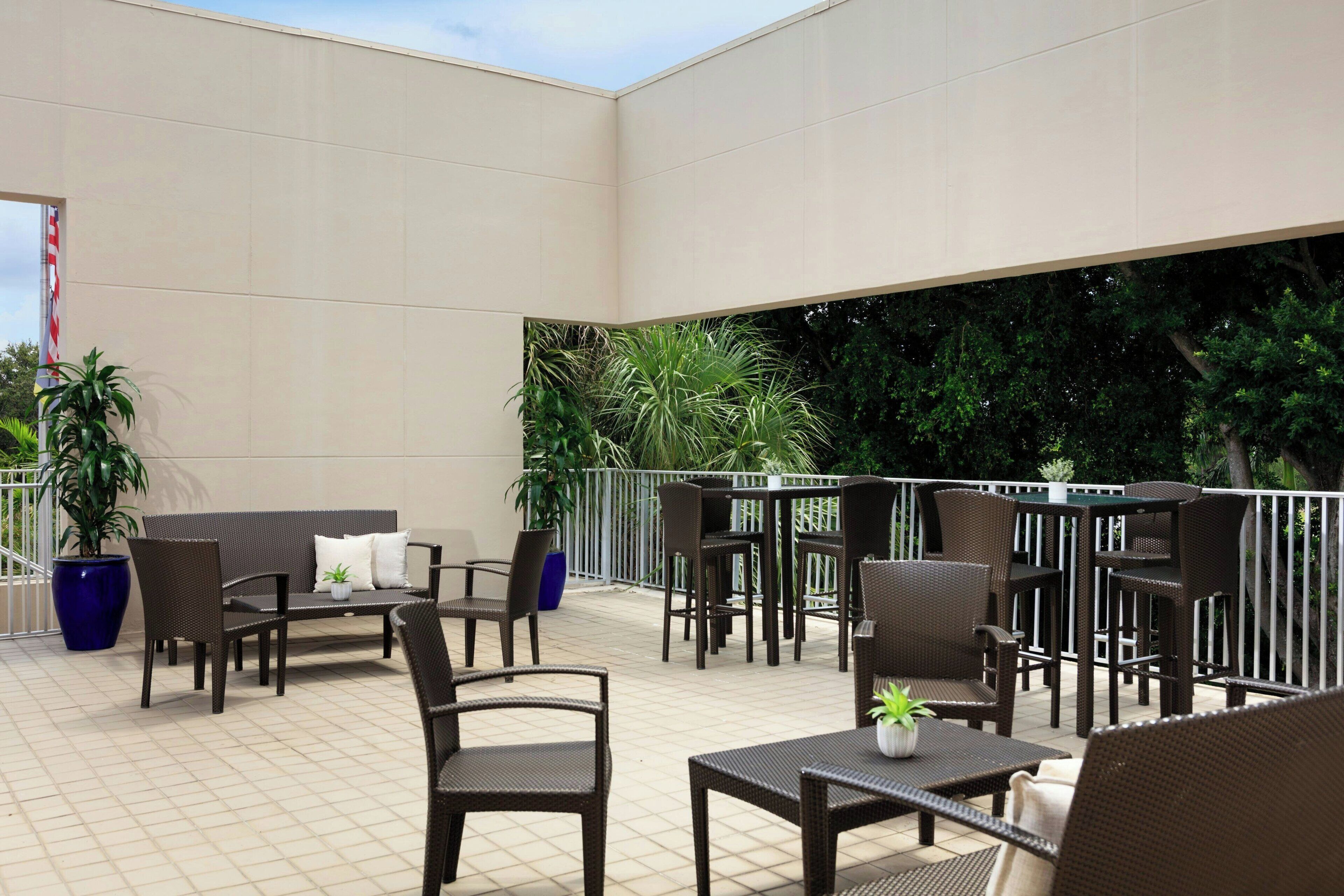 Un espace extérieur aménagé en terrasse, avec des meubles en osier, des plantes en pot et une vue sur la verdure environnante.