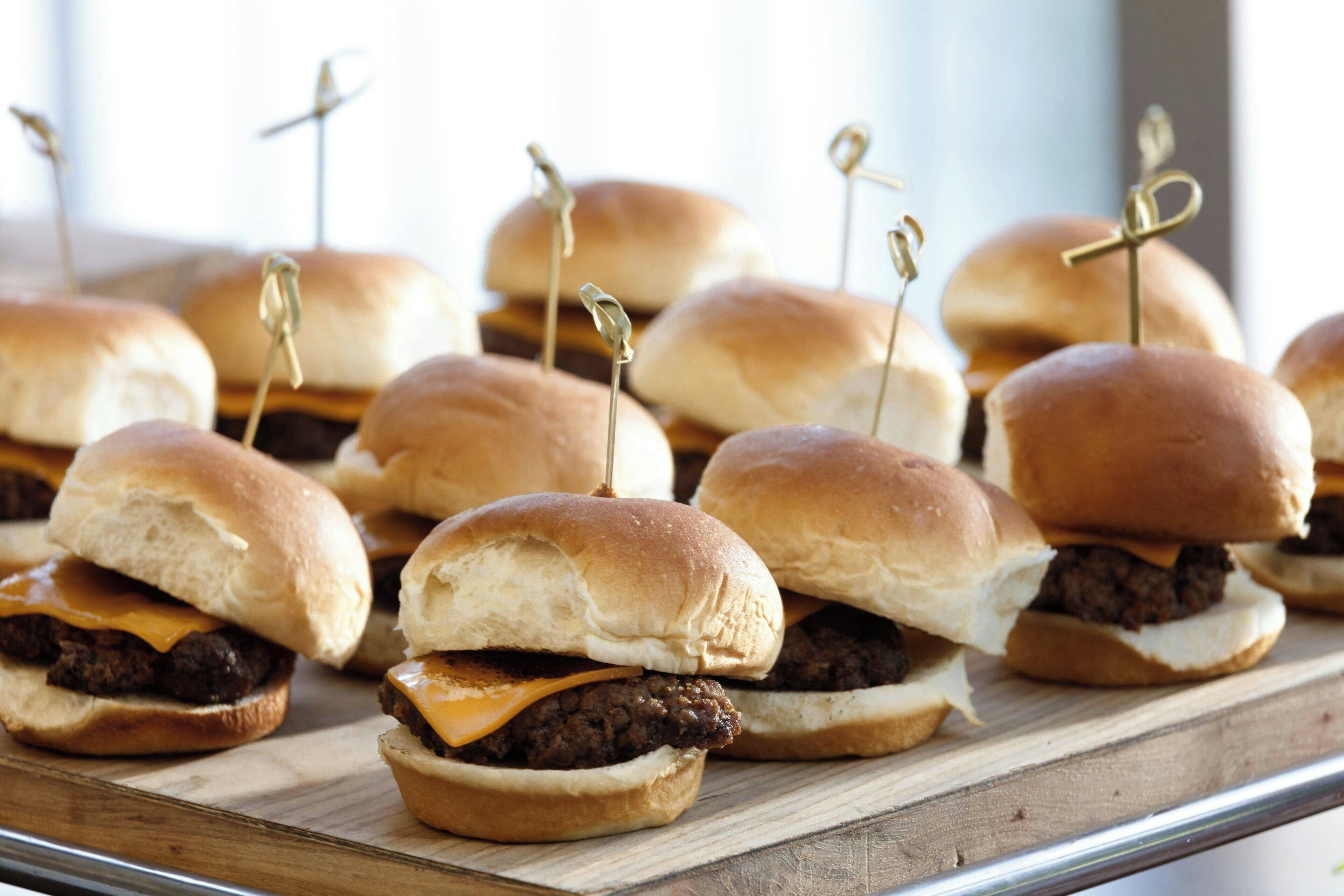 A tray of mini burgers with toothpicks, arranged on a wooden board.