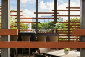 Un espace extérieur aménagé avec des chaises et des tables en osier, offrant une vue sur la verdure et les bâtiments, et agrémenté d’un élément décoratif aquatique en arrière-plan.