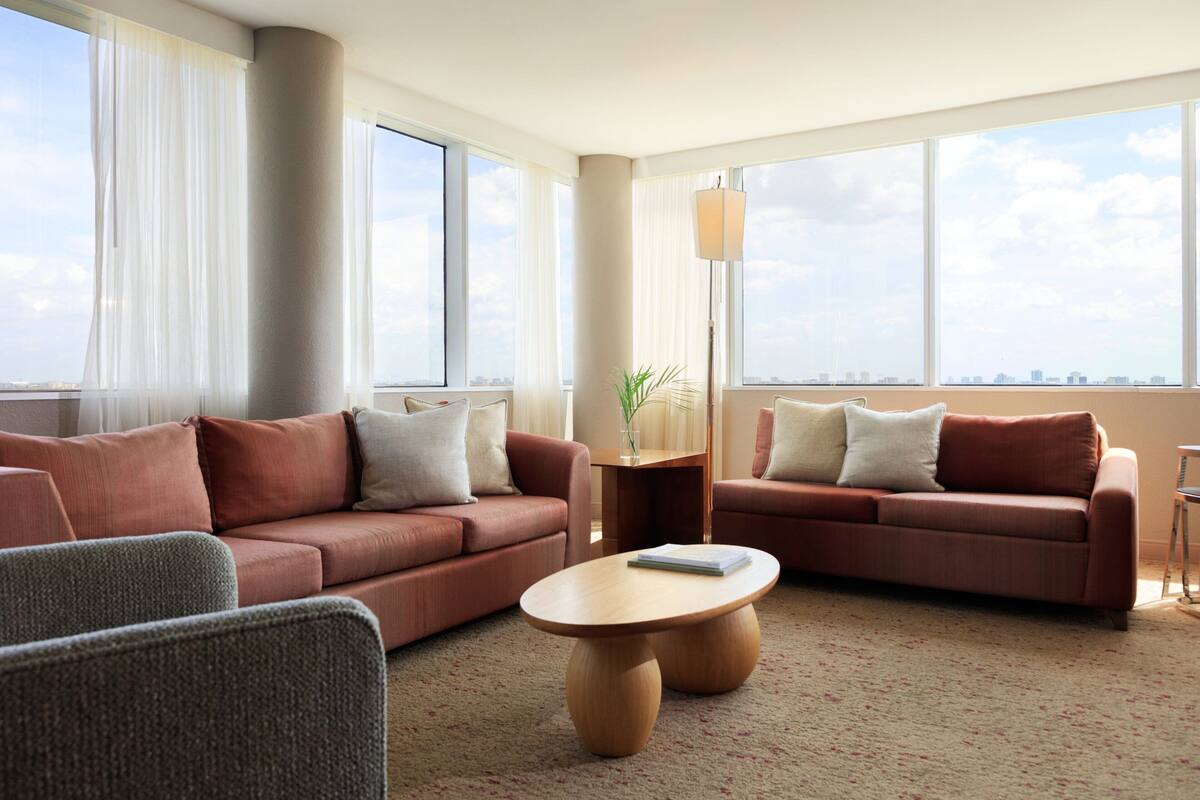 A modern hotel room with two sofas, a coffee table, and large windows offering a city view.