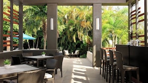 An outdoor patio area with wicker furniture, a bar, and lush greenery.