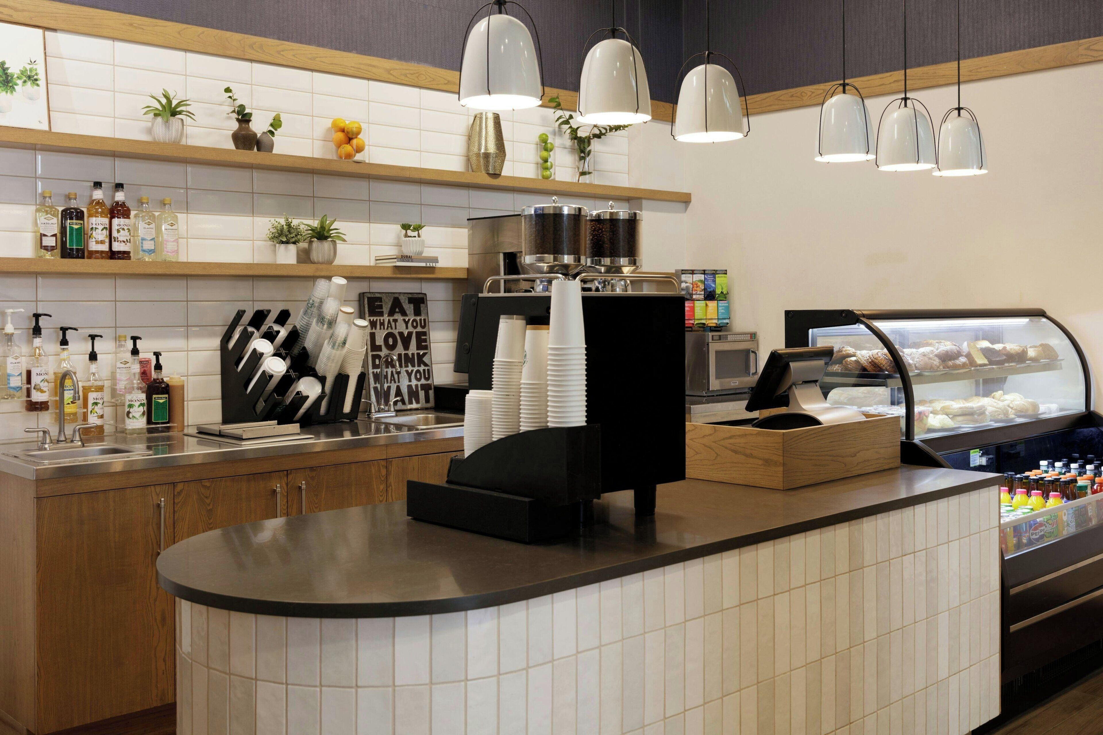Una cafetería con mostrador, máquinas de café y una vitrina con pasteles.