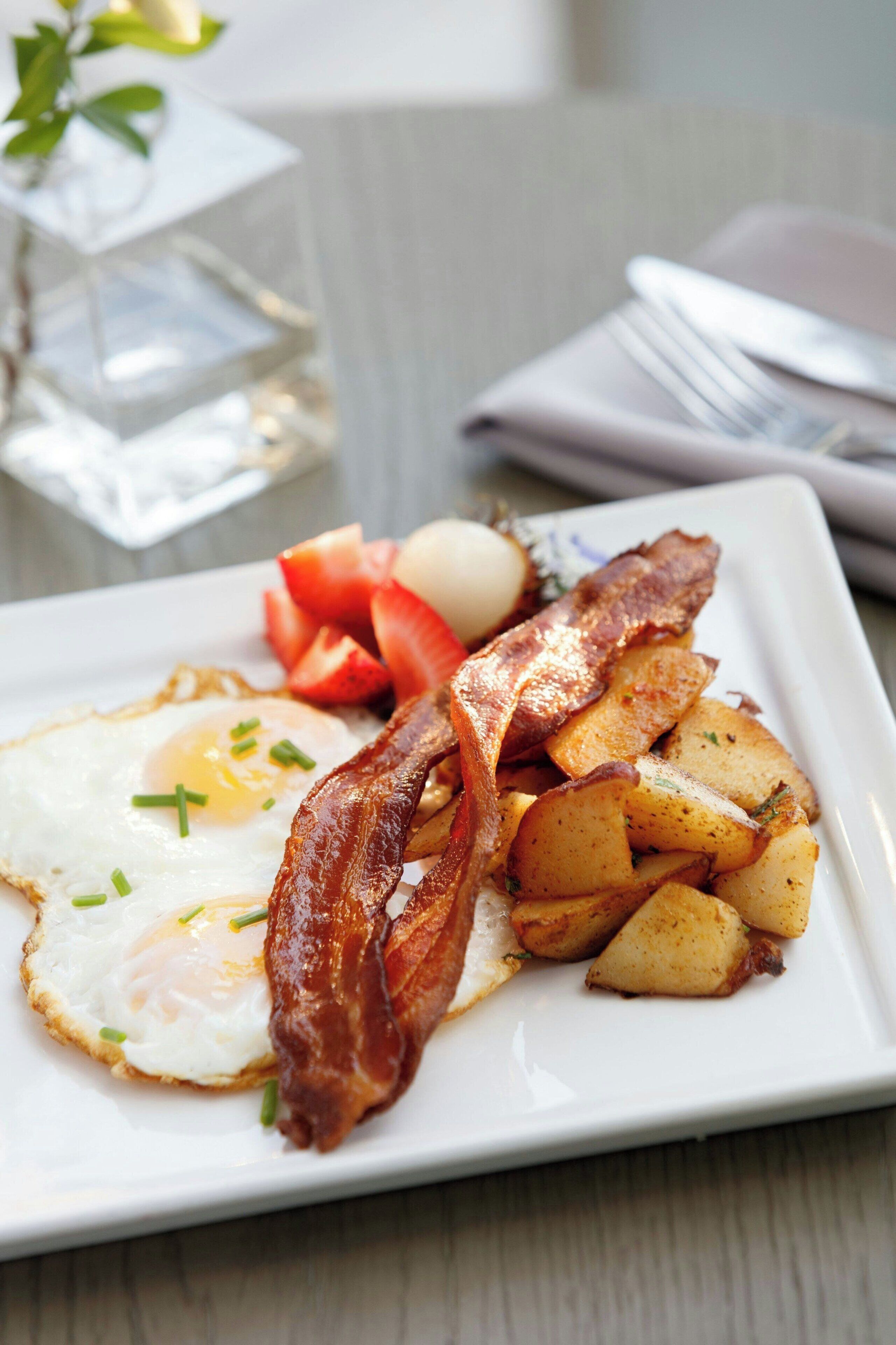 Ein Teller Frühstück mit Eiern, Speck, Kartoffeln und Tomaten.