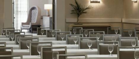 A conference room with rows of tables and chairs, each with a wine glass.