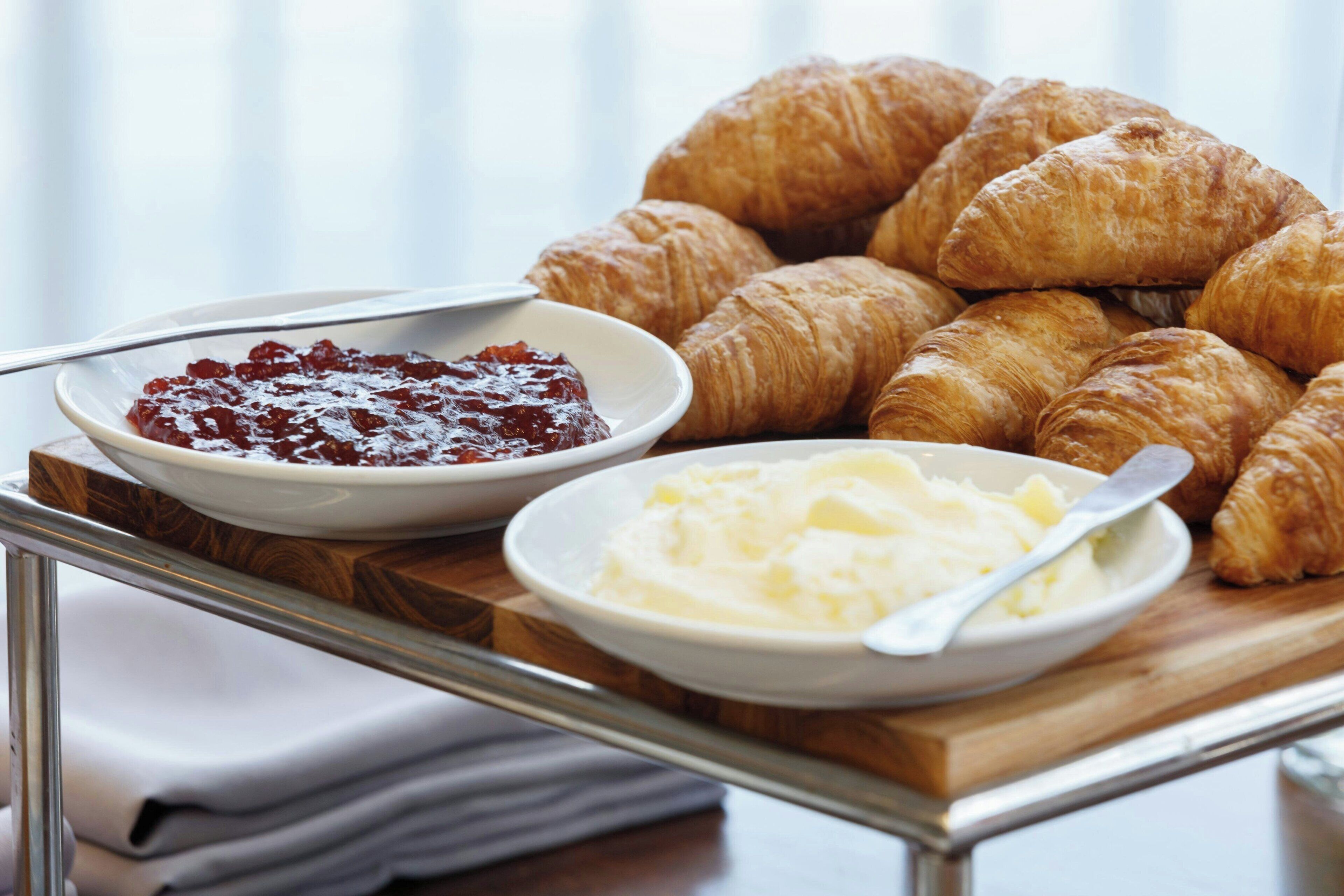 Un plateau avec des croissants et deux bols de nourriture, l’un contenant de la confiture et l’autre du beurre.