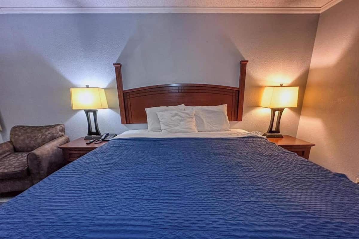 A hotel room with a large bed, two bedside lamps, a chair, and a telephone on the nightstand.