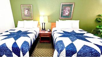 A hotel room with two beds, each with a blue and white quilt, a nightstand with a lamp, and two framed pictures on the wall.