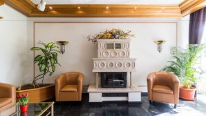 A lobby with a fireplace, two leather armchairs, a glass coffee table, and potted plants.