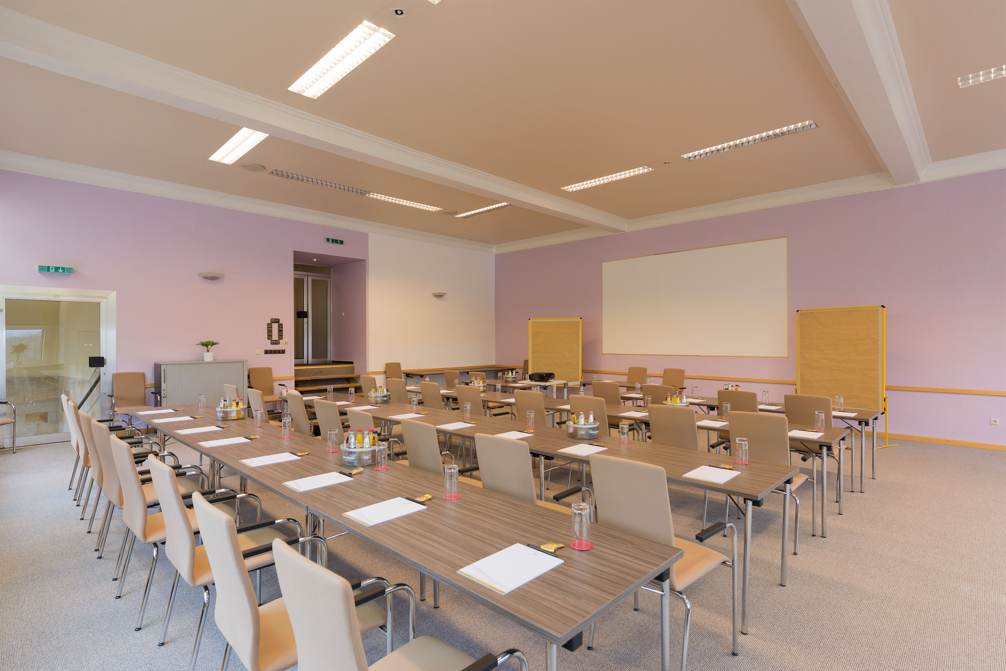 A conference room with long tables, chairs, a projector screen, and a whiteboard.