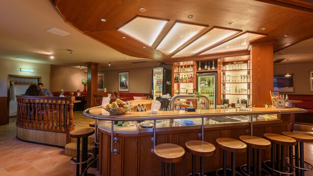 A bar area with a wooden bar counter, stools, and a variety of bottles and glasses.