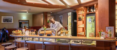A bar area with a bartender, wooden bar counter, stools, and shelves with bottles.