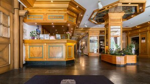 A hotel lobby with a reception desk, wooden paneling, and a black doormat with the hotel's name.
