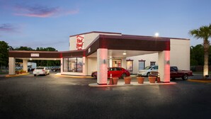 A Red Roof gas station with multiple fuel pumps, a covered parking area, and a clear sky.