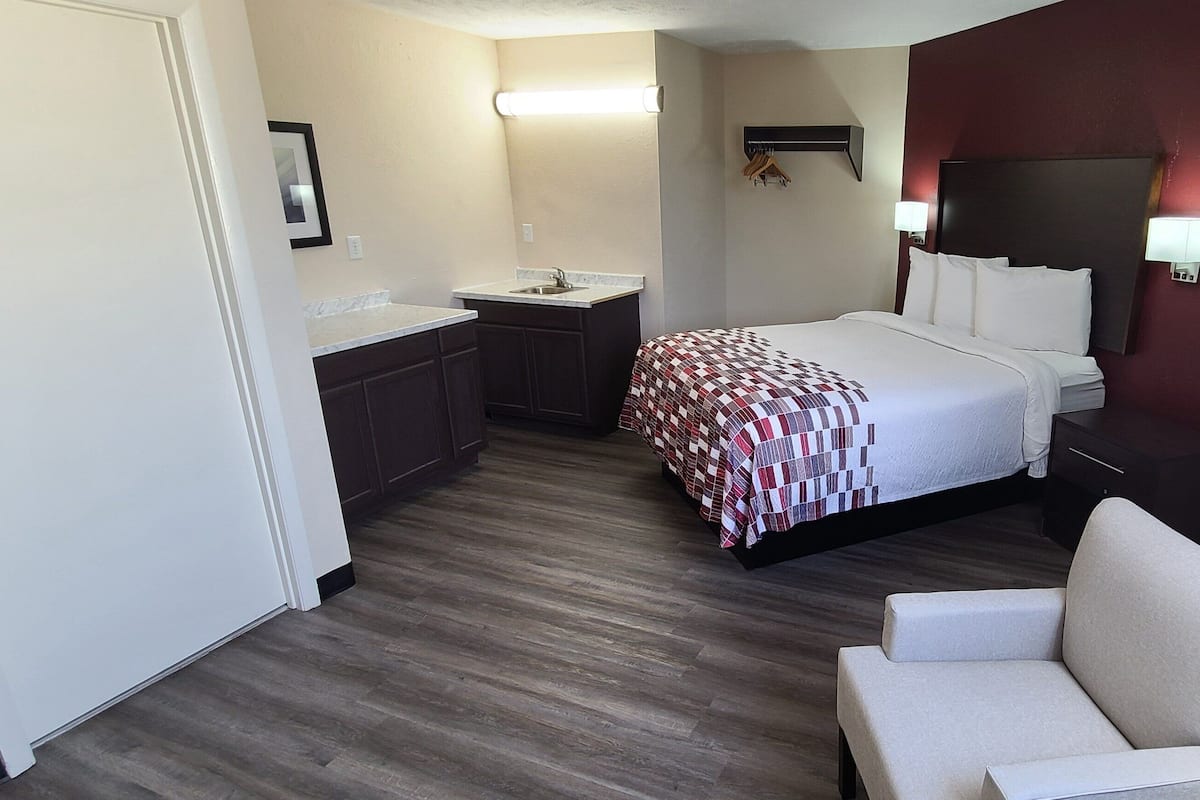 A hotel room with a bed, a small desk, a chair, a nightstand, a mirror, and a window with curtains.