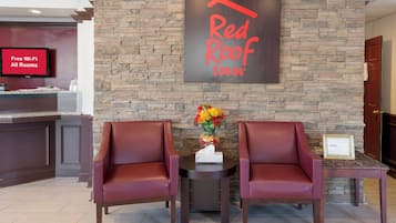 Zona de recepción de Red Roof Inn con un fondo de pared de piedra, dos sillones de cuero, un jarrón con flores y un cartel que indica Wi-Fi gratuito en todas las habitaciones.