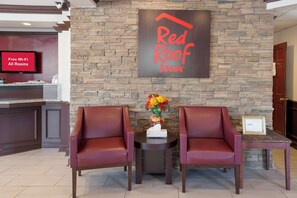A Red Roof Inn reception area with a stone wall backdrop, two leather chairs, a vase with flowers, and a sign indicating free Wi-Fi in all rooms. - Red Roof Inn Dillon, SC (Dillon)