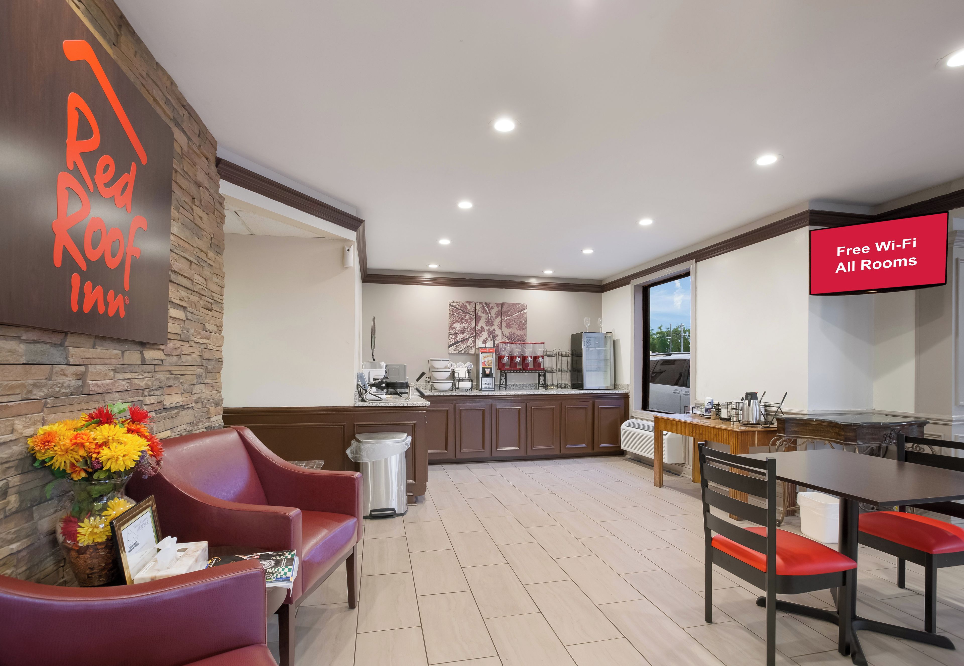 A hotel lobby with a reception desk, a seating area with chairs, a kitchenette, and a dining area with a table and chairs.