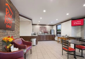 A hotel lobby with a reception desk, a seating area with chairs, a kitchenette, and a dining area with a table and chairs.