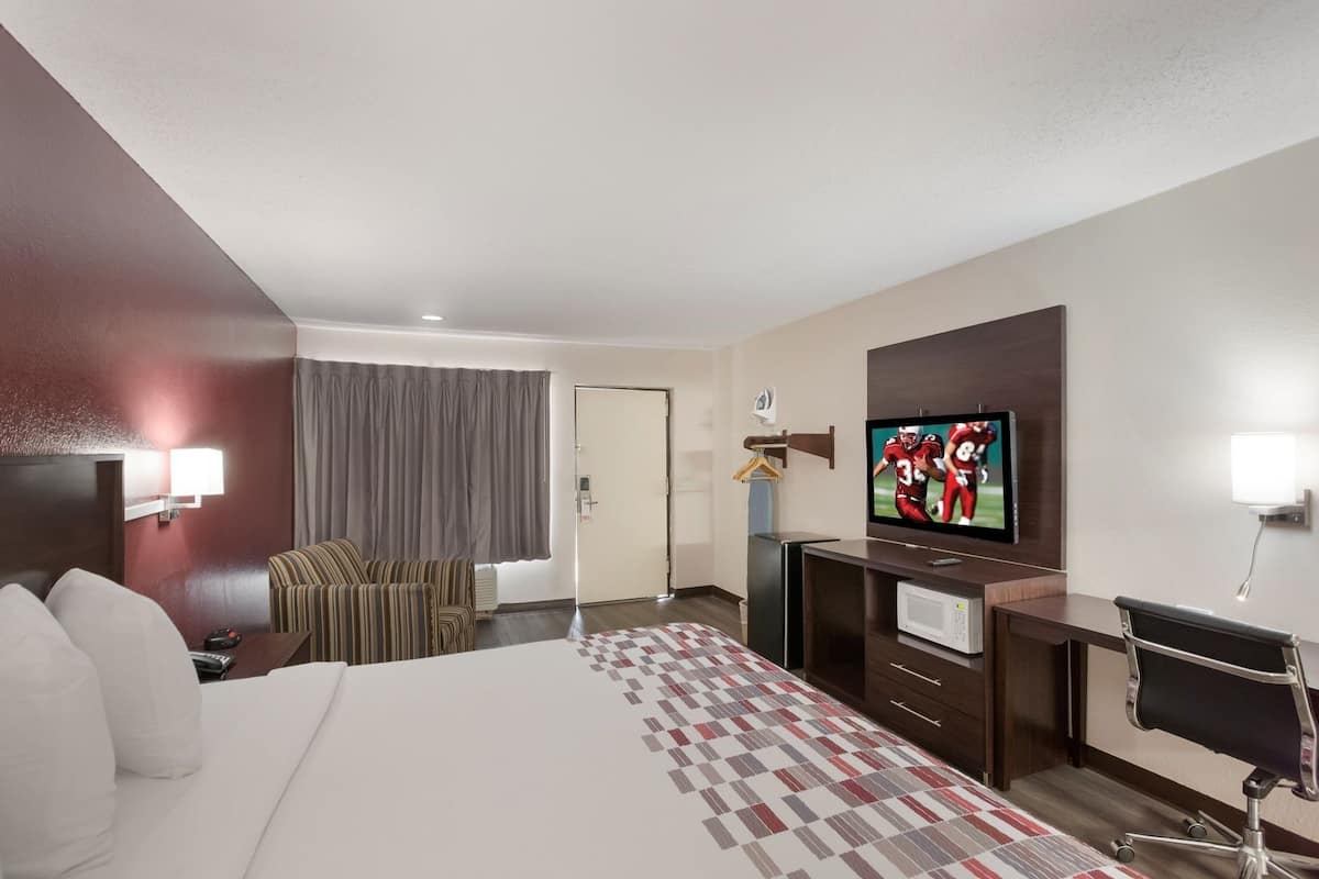 A hotel room with a bed, a desk, a TV, a chair, and a window with curtains.